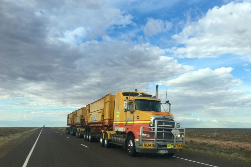 Semi-truck driving down an open rural highway, carrying a full truckload.
