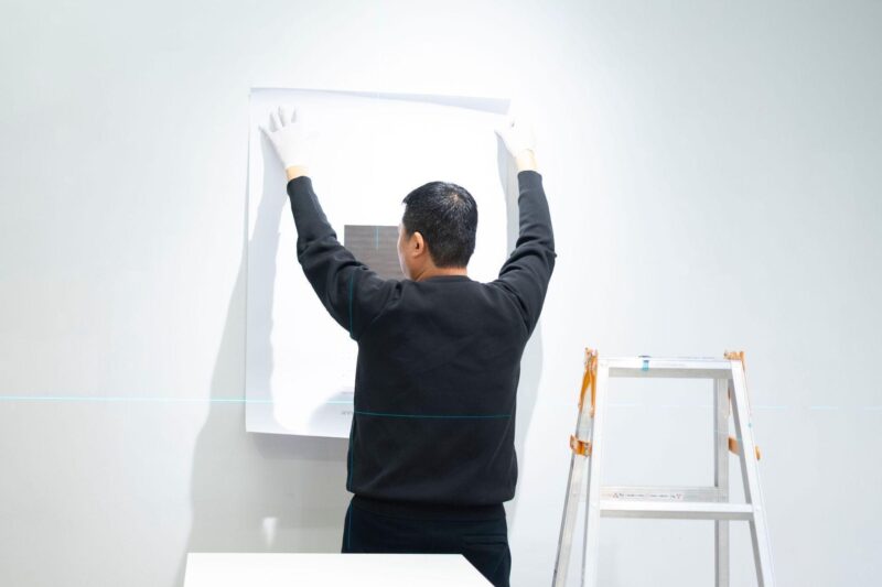 Gallery installer wearing protective gloves carefully mounting artwork on a wall, illustrating professional art handling and installation services.